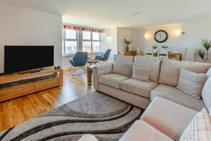 A modern living room with a flat-screen TV, a beige sofa, and a dining area with a table and chairs. - 3 Bed in Newquay (oc-o32258) (Newquay)