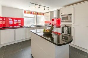 A modern kitchen with white cabinets, a black countertop, and stainless steel appliances. - 3 Bed in Newquay (oc-o32258) (Newquay)