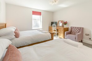 A bedroom with two beds, a desk, a chair, and a window with a red blind. - 3 Bed in Newquay (oc-o32258) (Newquay)