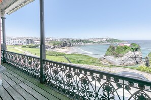 A balcony with a view of a coastal town, a rocky shoreline, and a body of water. - 3 Bed in Newquay (oc-o32258) (Newquay)