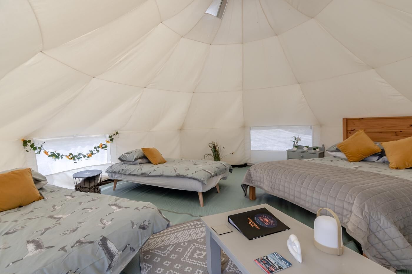 A spacious tent with three beds, a table with a book and a lamp, and a window with a view.