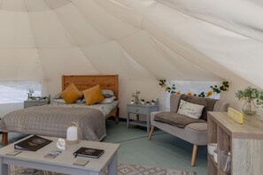 A cozy tented accommodation with a bed, a seating area, and a table with books and a candle.