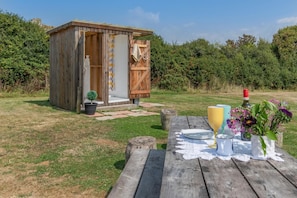 A wooden structure with a door, a picnic table with plates and a bottle, and a potted plant.