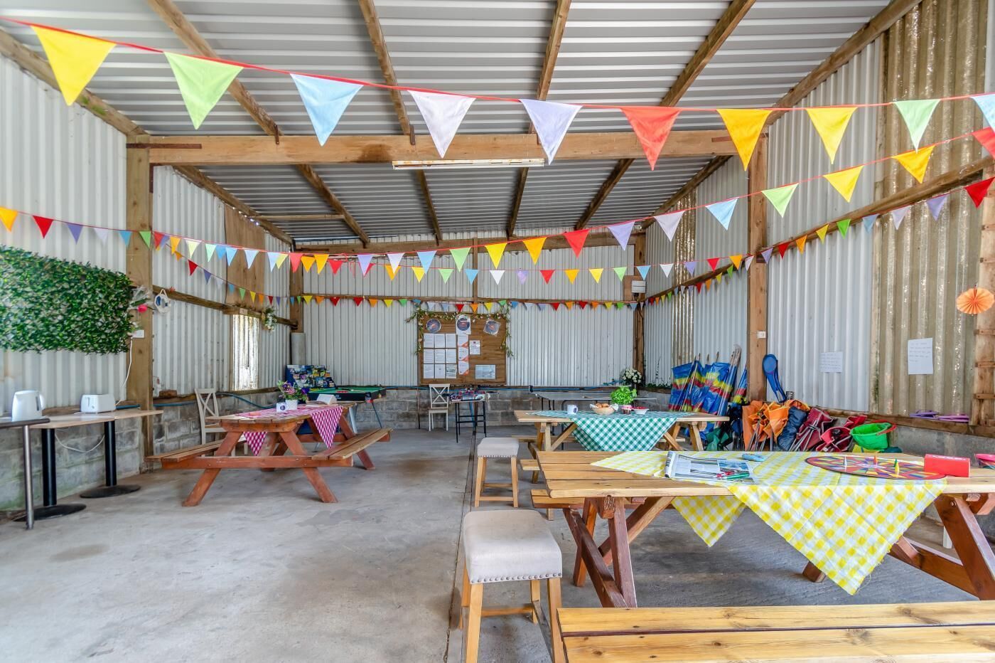 Ein rustikaler Raum im Stil eines Stalls mit Holztischen und -bänken, bunten Wimpeln und verschiedenen Ausstellungsstücken.