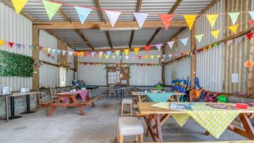 Ein rustikaler Raum im Stil eines Stalls mit Holztischen und -bänken, bunten Wimpeln und verschiedenen Ausstellungsstücken.