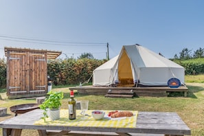 A tent with a platform, a wooden outhouse, a picnic table with food and drinks, and a sign with the name 'LINDSWAY'.