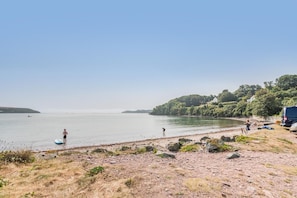 A beach with a clear sky, a person standing with a surfboard, and a vehicle parked on the shore.