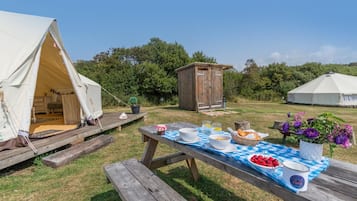 Un terrain de camping avec une tente, une table en bois dressée pour un repas et une petite structure en bois.