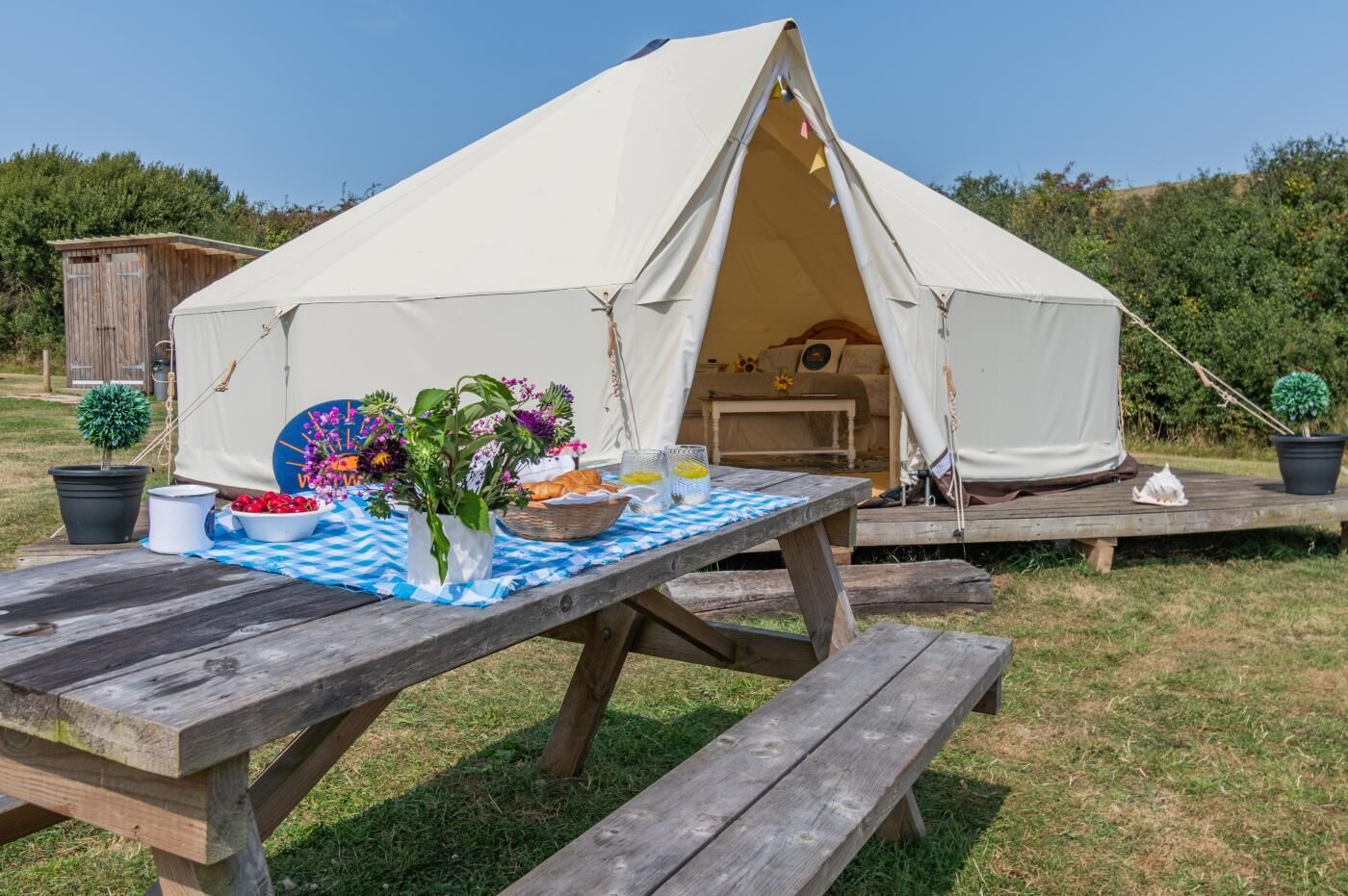 Een tent met een picknicktafel ervoor, omringd door groen.