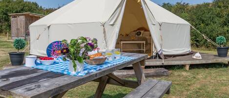 A tent with a picnic table set up in front, surrounded by greenery.