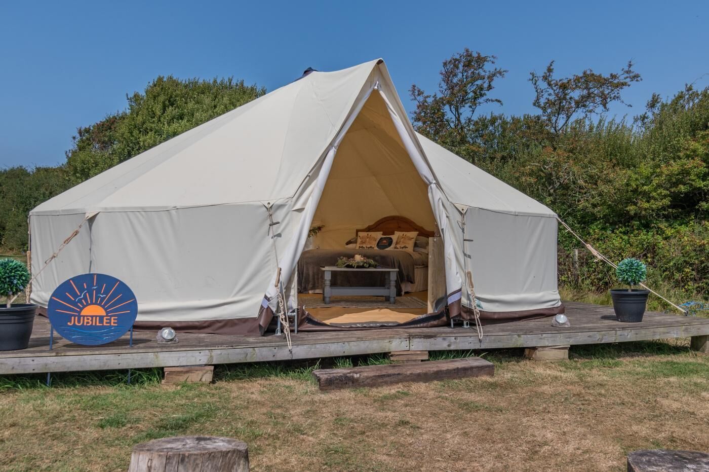 Een koepelvormige tent met een bed erin, omringd door een houten terras en potplanten.