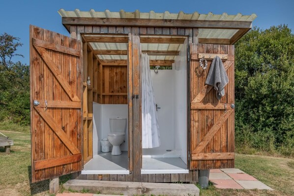 A wooden outdoor toilet with a white toilet and a shower curtain.