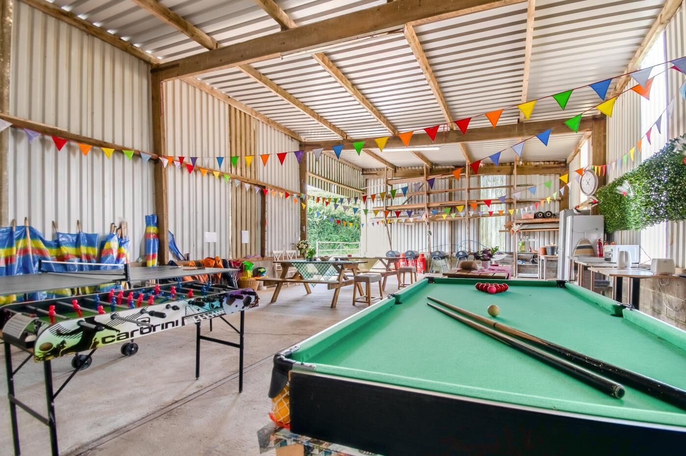 Een overdekte recreatieruimte met een tafelvoetbaltafel, pooltafel en zithoek.