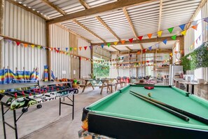 Un espace de loisirs intérieur comprenant une table de baby-foot, une table de billard et un coin salon.