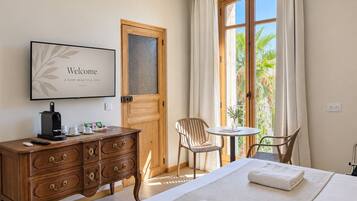 A hotel room with a bed, a desk with a coffee maker, a chair, a small table, and a window with curtains.