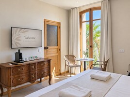 Habitación de hotel con cama, escritorio con cafetera, una silla, una mesita y una ventana con cortinas.