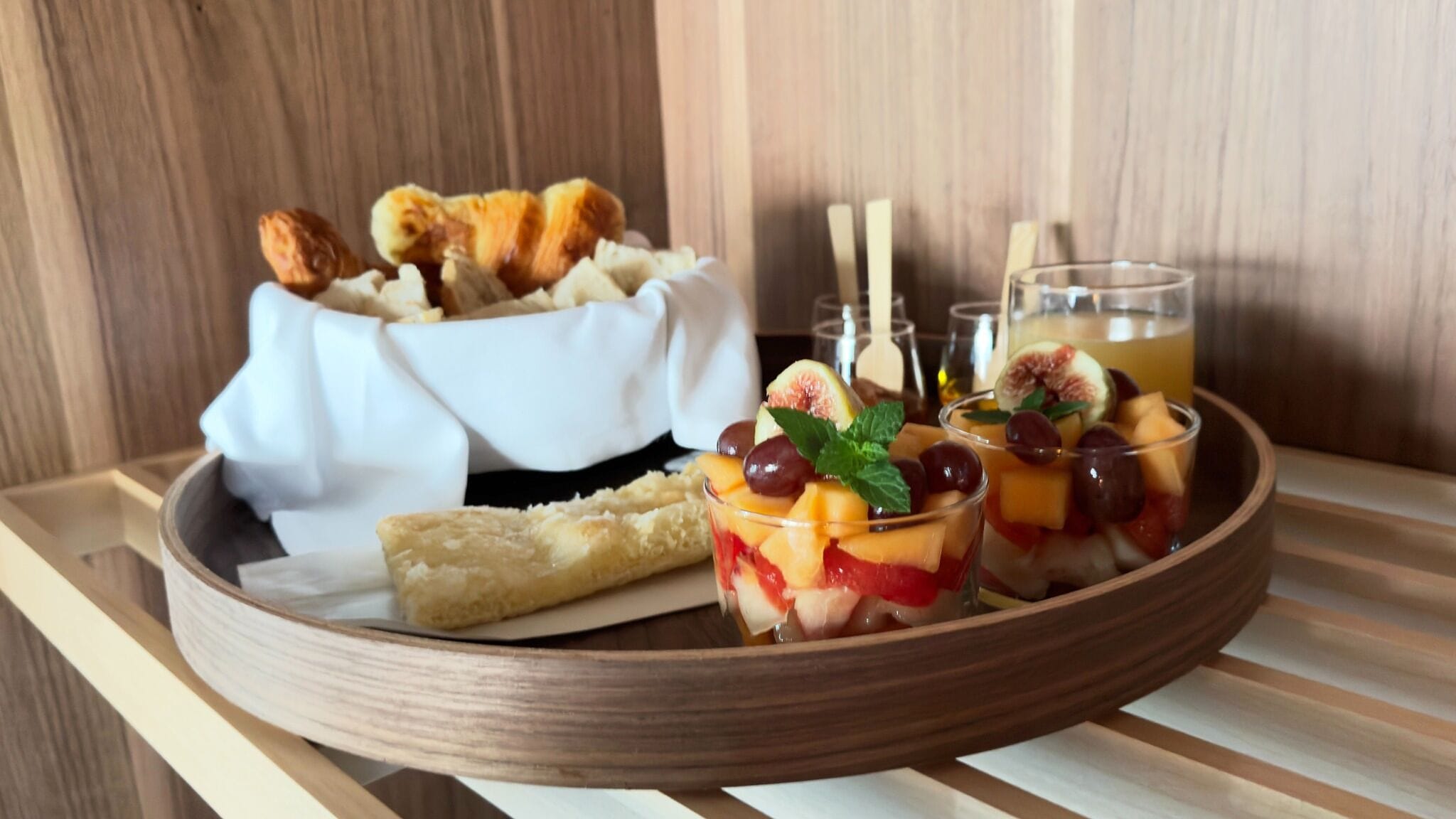 A wooden tray with a dessert, a glass of drink, and a bowl of bread.