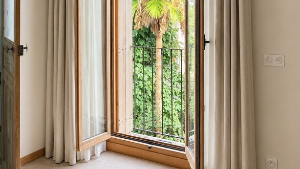 Una habitación con un ventanal, cortinas y vistas al exterior entre vegetación.