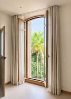 Una habitación con un ventanal, cortinas y vistas al exterior entre vegetación.