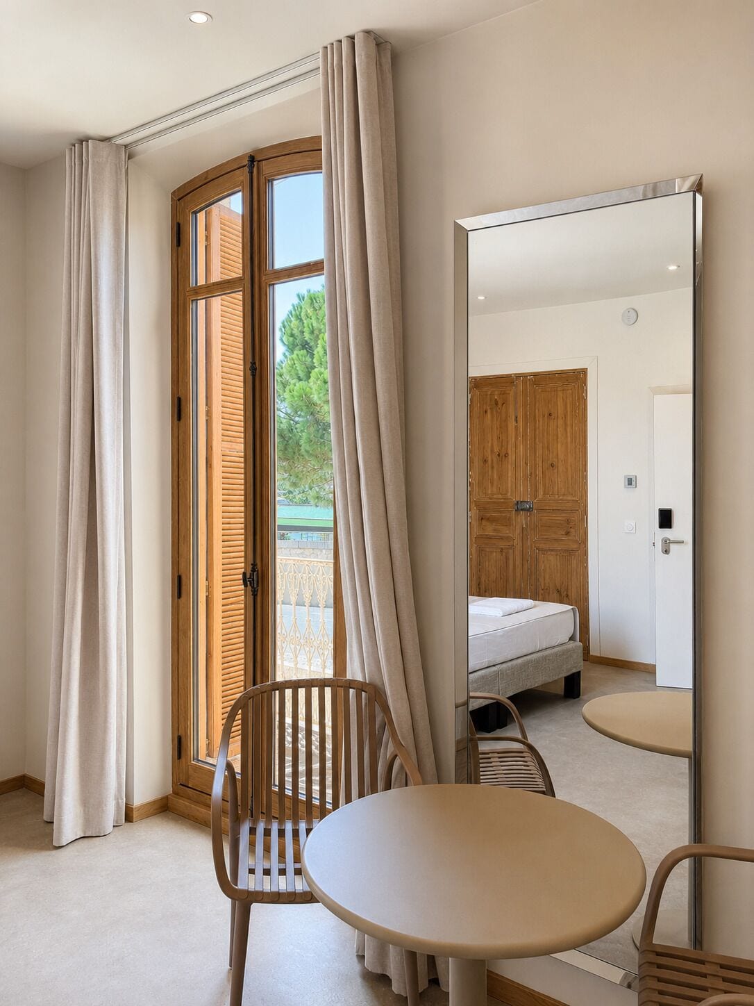 Una habitación de hotel con una cama, una mesa redonda, una silla y un espejo grande.