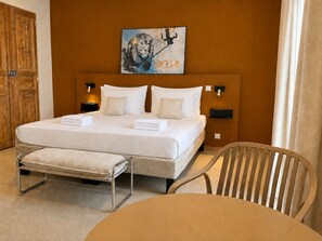 Habitación de hotel con una cama grande, mesitas de noche, una silla y un cuadro en la pared.