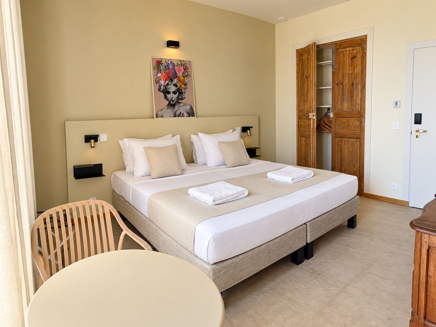 A hotel room with a bed, bedside tables, a chair, a round table, and a wooden wardrobe.