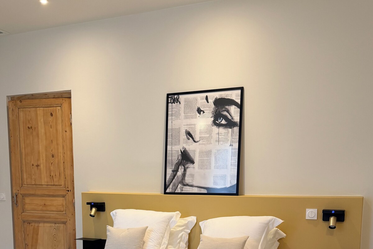 A hotel room with a large bed, a wooden wardrobe, a wall-mounted artwork, and bedside lamps.