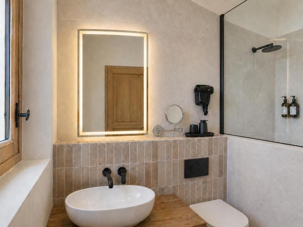Uma casa de banho moderna com um espelho grande, uma sanita redonda, uma sanita e uma cabine de duche.