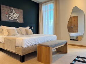 A modern bedroom with a large bed, bedside tables, a bench, a wall-mounted mirror, and a painting. - Le Palmier Aigues-Mortes Petite Camargue (Aigues-Mortes)