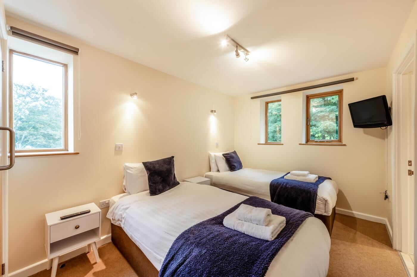 A hotel room with two beds, a TV, and a window with a view of trees.
