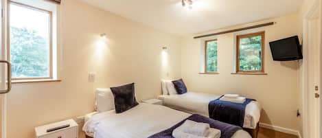 A hotel room with two beds, a TV, and a window with a view of trees.