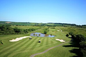 Ein Golfplatz mit Sandbunkern, einem Teich und blauem Himmel.