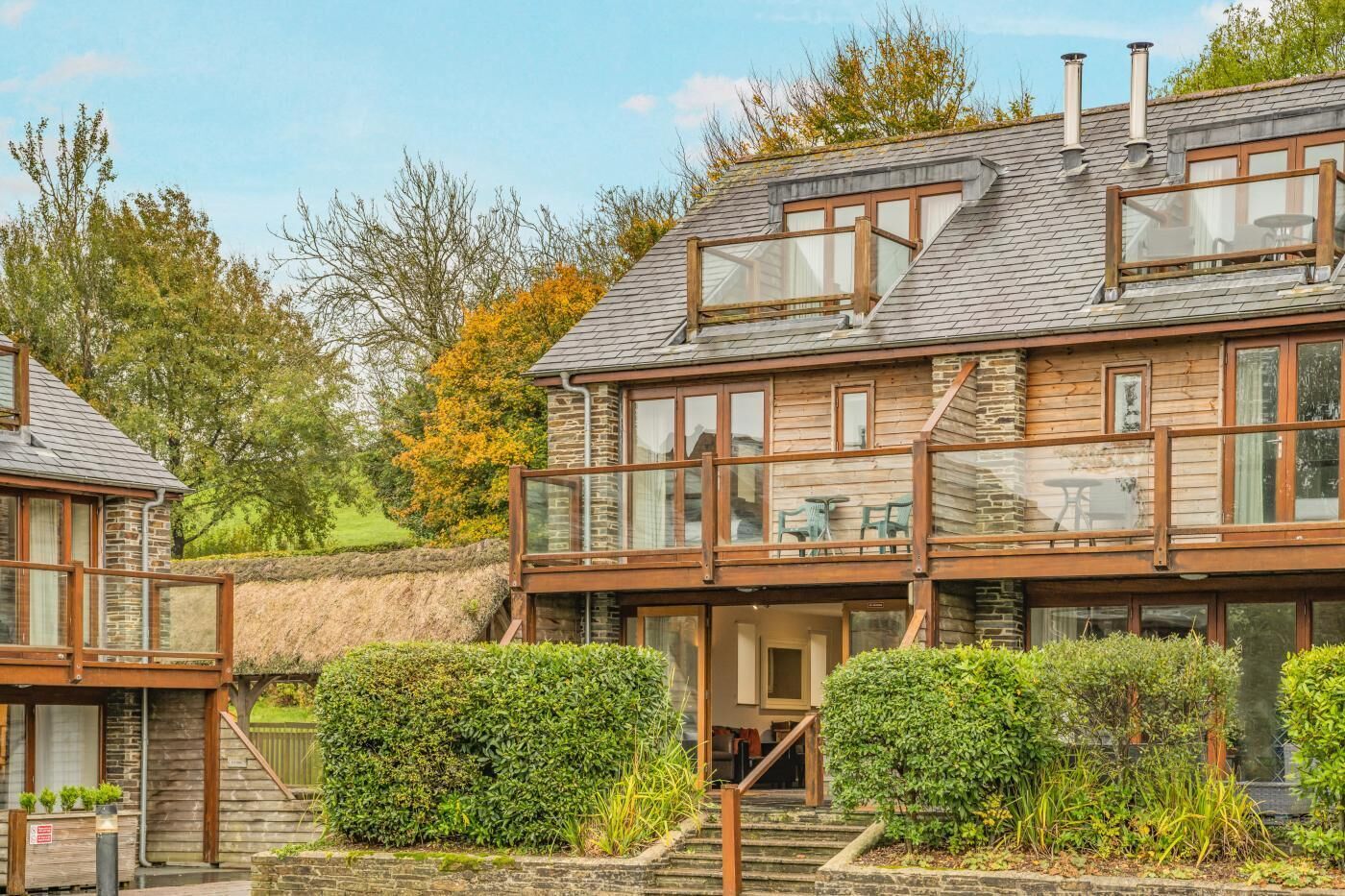Une maison à deux étages dotée d’un balcon, de murs en pierre et d’un toit de chaume.