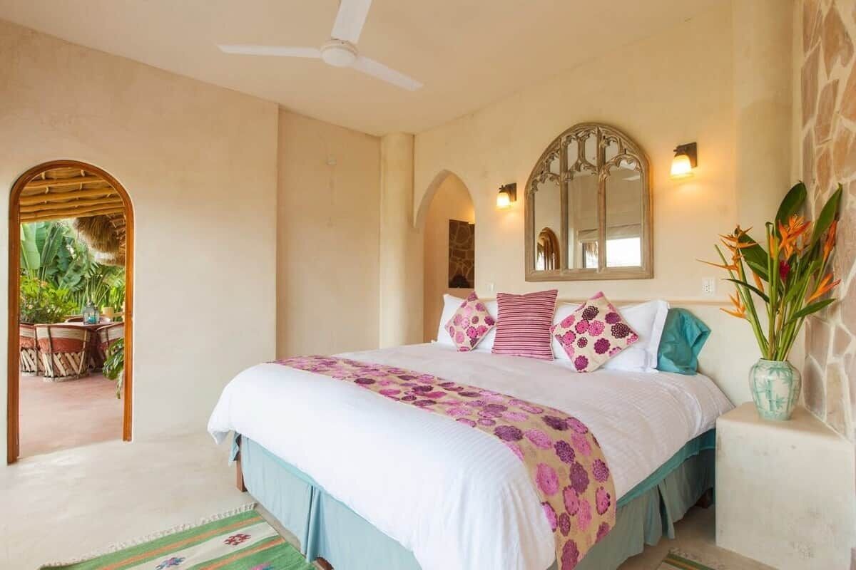 A bedroom with a bed, a ceiling fan, a mirror, and a potted plant.