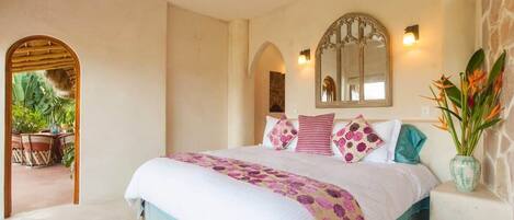 A bedroom with a bed, a ceiling fan, a mirror, and a potted plant.