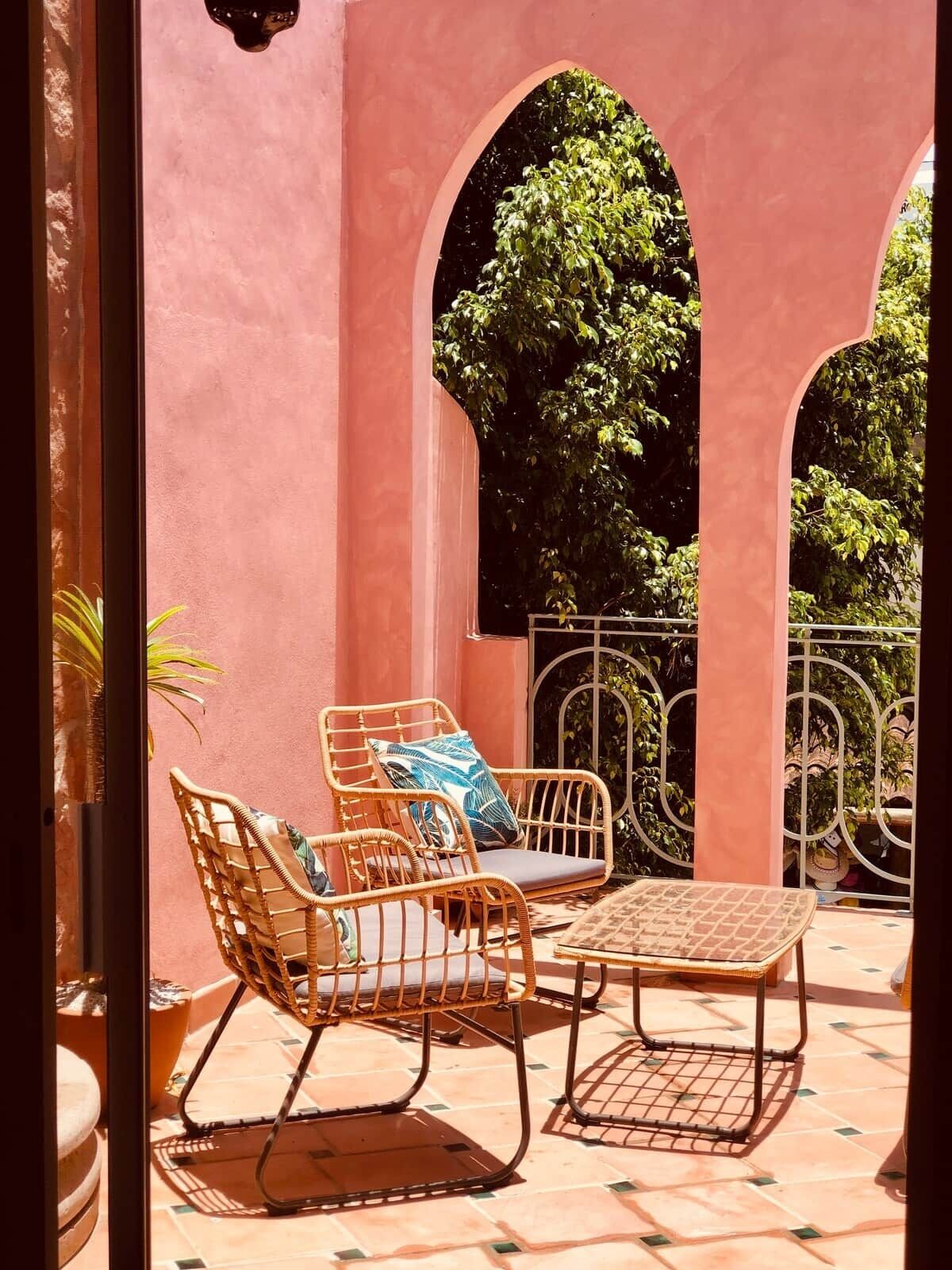 A patio with wicker furniture, a tiled floor, and a view of trees through arches.
