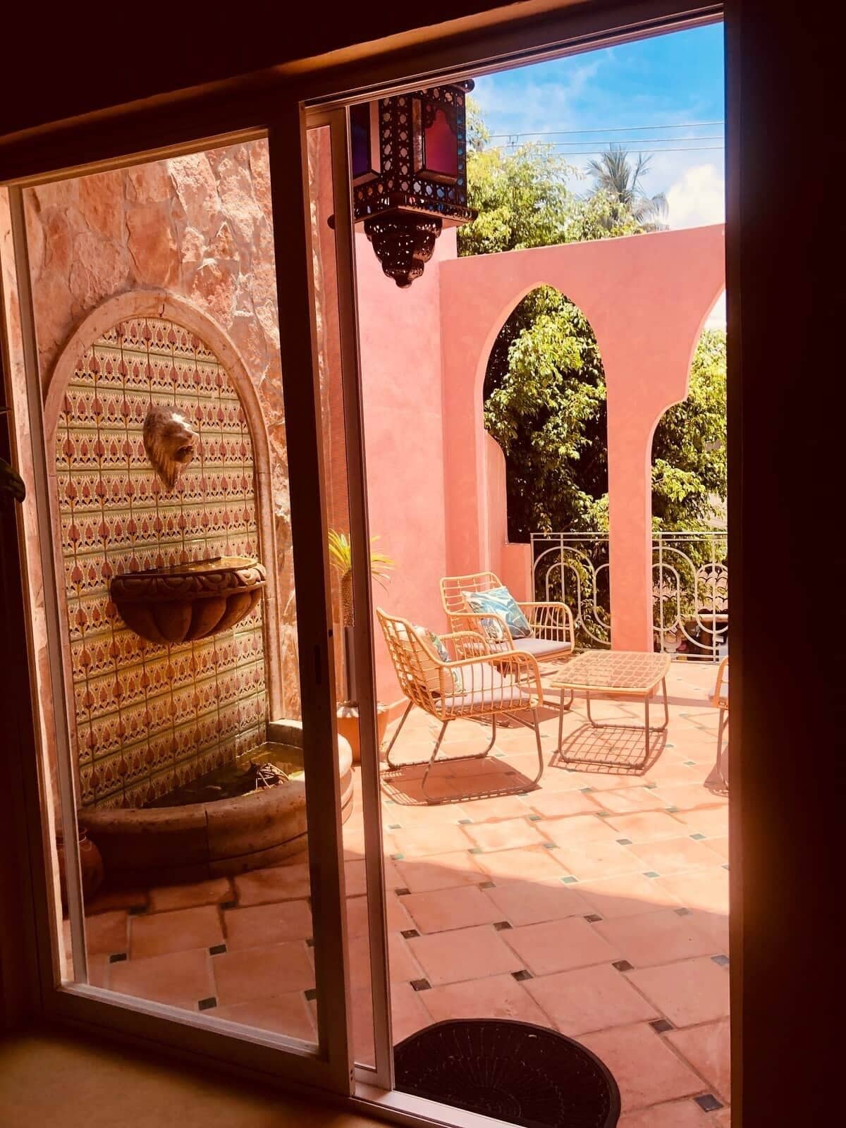 Interieur van een kamer met een betegelde muur, een hangende waterattractie, en uitzicht op een terras met meubilair.