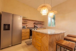 A kitchen with a central island, wooden cabinets, a stainless steel refrigerator, and pendant lighting. - Bella Rosa, center of town, steps to the beach. (San Francisco)