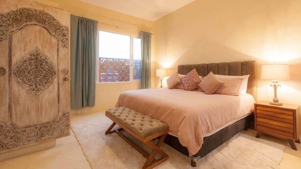 A bedroom with a large bed, bedside lamps, a bench, and a decorative door. - Bella Rosa, center of town, steps to the beach. (San Francisco)