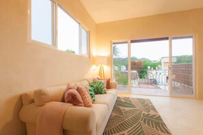A living room with a sofa, a lamp, and a view through a sliding glass door to an outdoor area with a railing. - Bella Rosa, center of town, steps to the beach. (San Francisco)