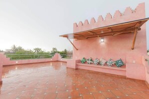 Eine Dachterrasse mit einer rosafarbenen Wand, einer Holzpergola und einer Sitzbank mit Kissen.