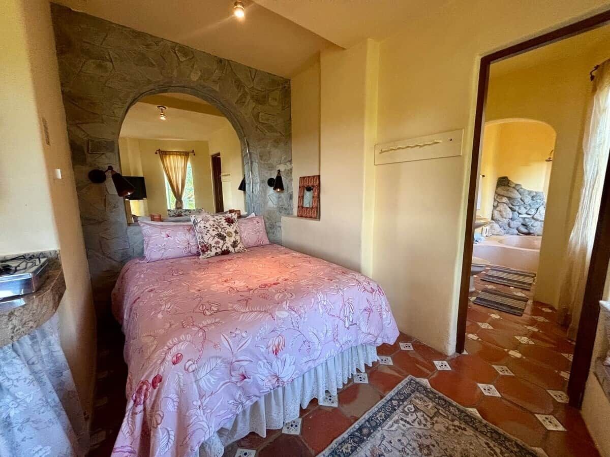 A bedroom with a stone archway, a bed with floral bedding, and a view of a stone wall.