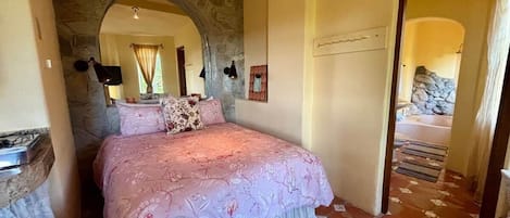 A bedroom with a stone archway, a bed with floral bedding, and a view of a stone wall.