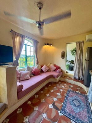 Ein Zimmer mit einer gebogenen Couch, einem Deckenventilator, einem Fernseher und einem gestreiften Boden.