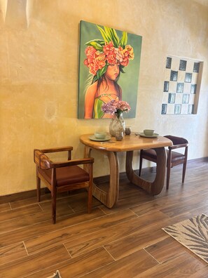 A dining area with a wooden table, two chairs, a vase with flowers, and a painting on the wall. - Romantic Jungle Bungalow w/ Pool Near Town & Beach (Sayulita)