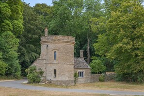 A stone tower with a small attached building, surrounded by dense trees. - 1 Bed in Cirencester (oc-r34615) (Cirencester)