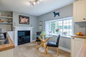 A modern kitchen with a fireplace, a dining table with chairs, and a window with a view. - 1 Bed in Cirencester (oc-r34615) (Cirencester)