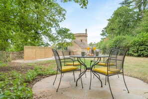 An outdoor patio with a round table and four chairs, a stone pathway, and a stone building in the background. - 1 Bed in Cirencester (oc-r34615) (Cirencester)