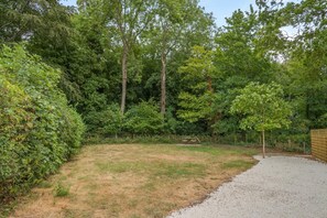 A grassy outdoor area with a gravel path, surrounded by dense trees and a wooden fence. - 1 Bed in Cirencester (oc-r34615) (Cirencester)