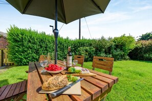 Een buitentafel met een fles wijn, glazen, een schaal druiven en een brood.